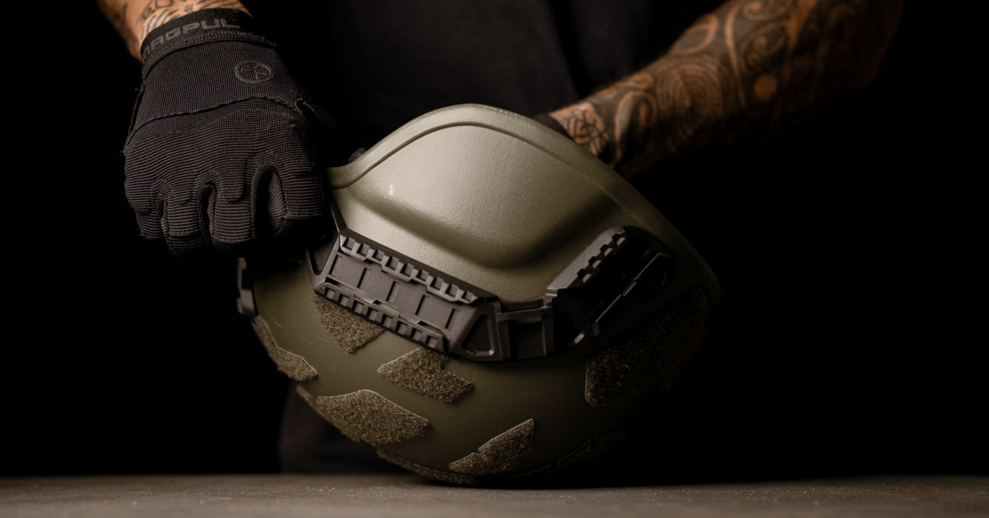 Person wearing a black glove holding a green tactical helmet